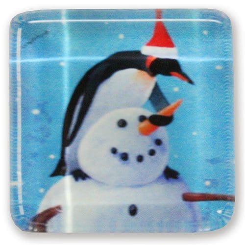 A square glass plate with a penguin and snowman on it, decorated with needlepoint magnets.