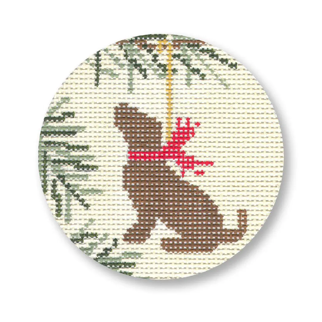A cross stitch ornament with a brown dog hanging from a pine tree, created by Cecilia Ohm Eriksen.