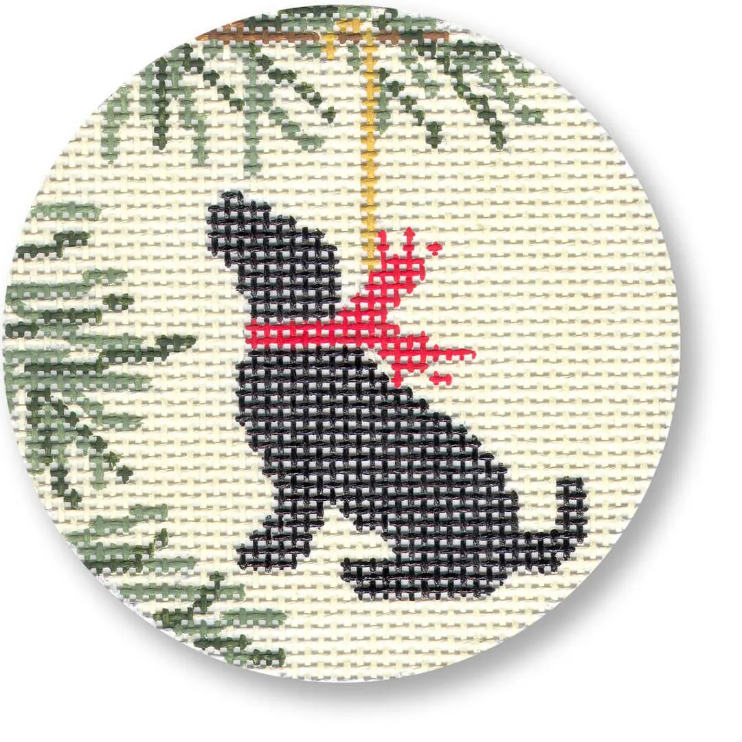A cross stitch pattern of a black dog hanging from a Christmas tree designed by Cecilia Ohm Eriksen.