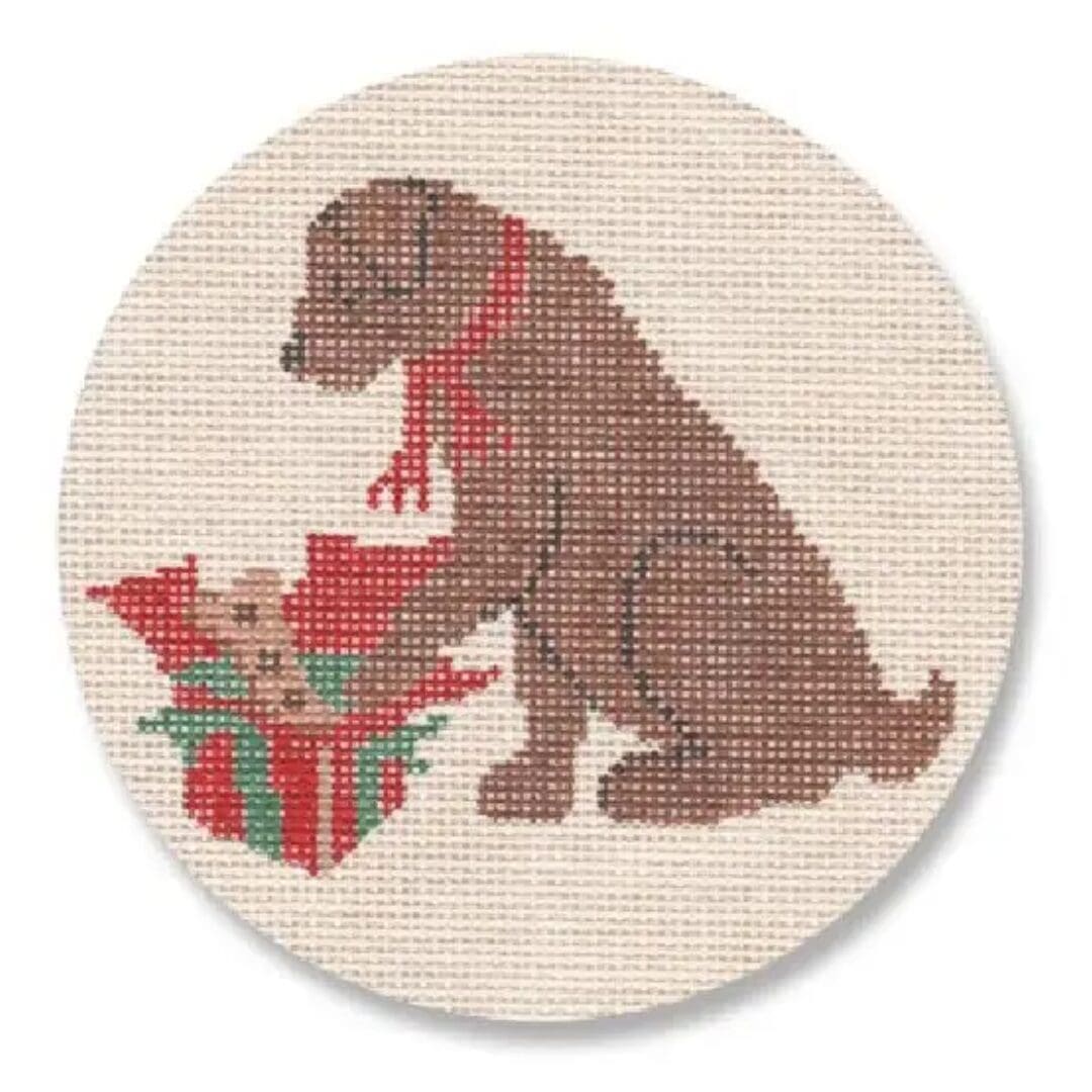 A cross stitch pattern of a brown dog with a gift designed by Cecilia Ohm Eriksen.